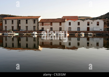 Riflessioni delle antiche concerie con tetti di tegole rosse sulla riva sud del fiume Temo a Bosa con barche ormeggiate e colline Foto Stock