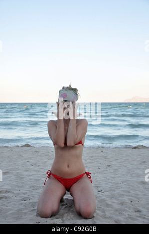 Metà donna adulta in bikini Inginocchiati sulla spiaggia che ricopre la faccia, Alcudia, Mallorca, Spagna, Europa Foto Stock