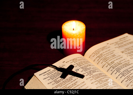 Crocifisso collana su una Bibbia aperta con candela illuminata Foto Stock