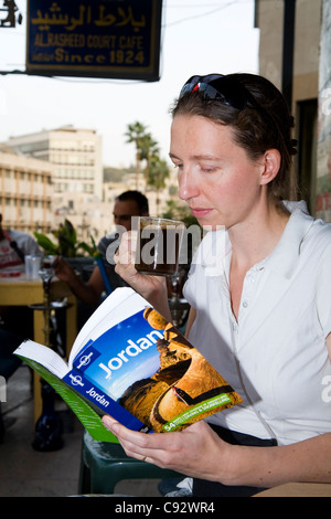 Turista legge la Lonely Planet guida viaggi in Giordania nel cafe sorseggiando una bevanda calda / tè o caffè. Amman, Giordania. Foto Stock
