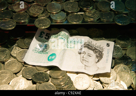 La deliberata restringere la messa a fuoco. Monete del Regno Unito e la testa della regina cinque Pound bank nota. Divertimento balneare penny arcade cade il gioco d'azzardo macchina Foto Stock