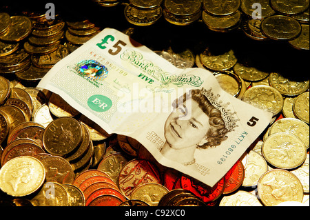 La deliberata restringere la messa a fuoco. Monete del Regno Unito e la testa della regina cinque Pound bank nota. Divertimento balneare penny arcade cade il gioco d'azzardo macchina Foto Stock