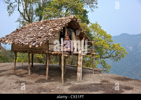 Un uomo si siede sulla veranda della sua piccola casa, sollevate su palafitte, situato in precario equilibrio sul bordo di una discesa ripida Foto Stock