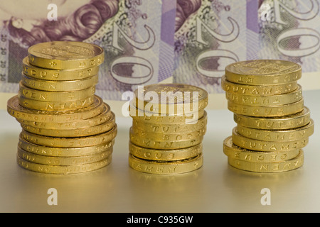 Uno e due libbre di monete in tre pile di fronte tre venti pound note Foto Stock