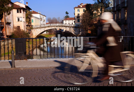 L'Italia, Veneto, Vicenza, Europa occidentale; una giovane donna di cicli su un ponte con 'Ponte San Michele" visibile in background Foto Stock