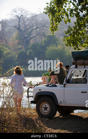 Il Malawi, Majete riserva faunistica. Famiglia su safari guardare fuori attraverso il fiume Shire dal loro veicolo di safari. Signor Foto Stock