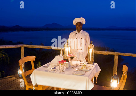 Il Malawi, il Parco Nazionale del Lago Malawi. Uno chef che si erge dalla tavola di cena sulla veranda chalet. Foto Stock