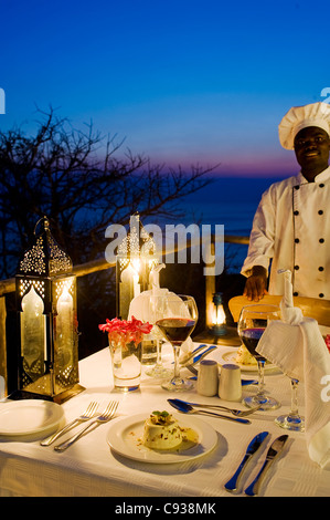 Il Malawi, il Parco Nazionale del Lago Malawi. Uno chef che si erge dalla tavola di cena sulla veranda chalet. Foto Stock
