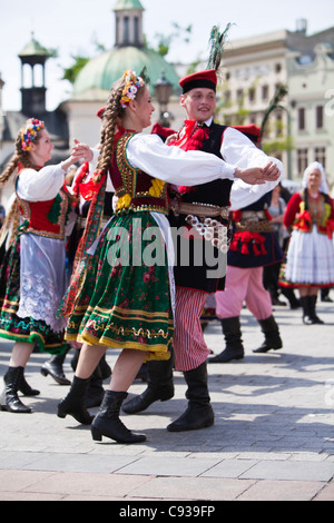 In Polonia, a Cracovia. Lucidare i ragazzi e le ragazze in costumi tradizionali balli in piazza del mercato. Foto Stock