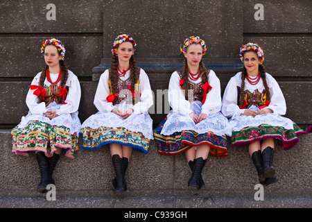 In Polonia, a Cracovia. Lucidare le ragazze in abito tradizionale udienza alla base di una statua. Foto Stock