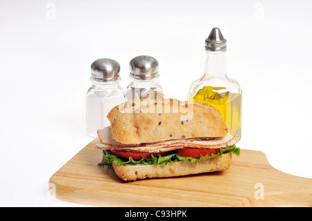 Pollo con lattuga e pomodoro sandwich in un rotolo su legno tagliere con condimenti di sale e pepe e olio di oliva su bianco Foto Stock