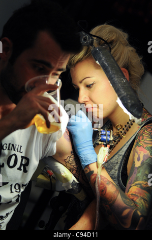 12.11.2011 Varsavia, Polonia. L uomo beve birra mentre donna tattooist opere su hie nuovo tattoo durante il primo giorno del tatuaggio, la verniciatura della scocca e pierceing show - 'arte del corpo convenzione" nel Palazzo della Cultura e della scienza a Varsavia. Foto Stock