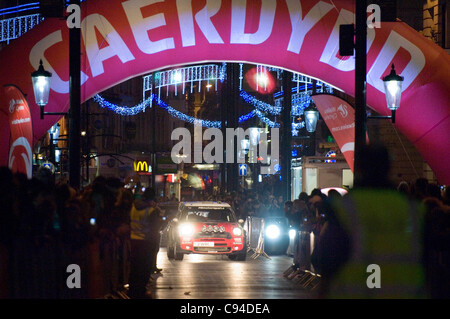 Kris Meeke (Gran Bretagna) e il suo co-pilota Paul Nagle (Irlanda) nel loro team WRC MINI John Cooper Works auto rendendo il loro modo attraverso il centro di Cardiiff stasera al giorno 3 della FIA WRC Rally Galles GB. Foto Stock