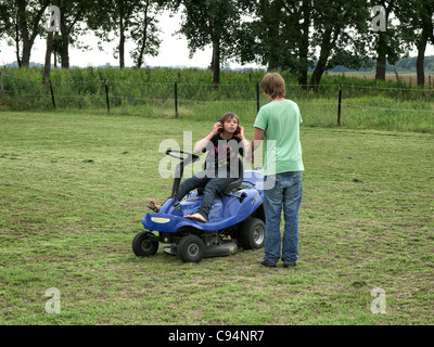 Due ragazzi la falciatura di un prato con un motore tosaerba in Horburg, Bassa Sassonia, Germania. Foto Stock