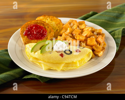 Una frittata al formaggio guarnita con panna acida e fette di avocado servito con patate e muffin inglese con jelly Foto Stock