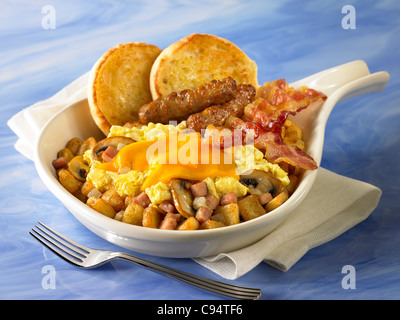 Una prima colazione la padella di patate, funghi e cipolle coperto con uova e formaggio e servita con pancetta, salsicce, muffin Foto Stock