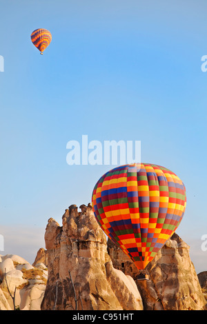 Due colorato arlecchino i palloni ad aria calda sul basso livello di volo attraverso la Cappadocia terreno di picchi di calcare la mattina presto sun Foto Stock