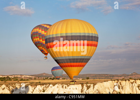 Tre paesaggio colorato i palloni ad aria calda a basso livello di volo su Cappadocia scogliere, la mattina presto il sole, cielo blu Foto Stock