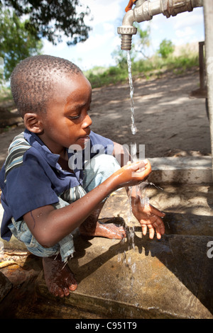 Un giovane bambino beve acqua da un pozzo a Dar es Salaam, Tanzania Africa Orientale. Foto Stock