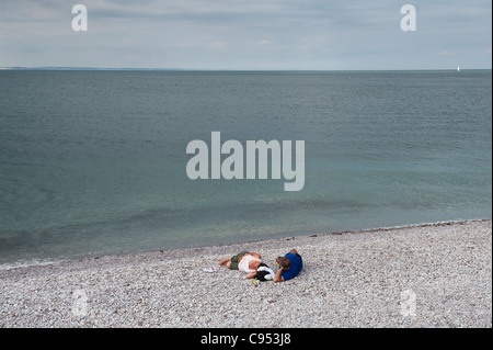 Una coppia di mezza età si trova decisamente sulla spiaggia di ghiaia sotto un cielo grigio e sovrastato a Brixham, Devon, Regno Unito Foto Stock