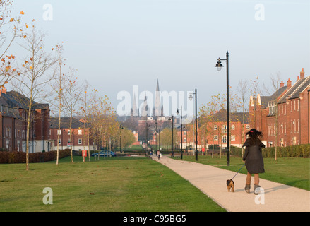 Lichfield Cathedral dalla cattedrale a piedi con alloggiamento moderno argento betulla alberi e pali della luce e la ragazza camminare il suo cane Foto Stock