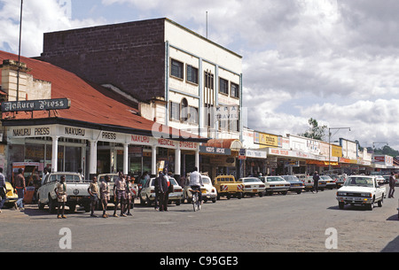 Strada principale Kenyatta Avenue nella città di Nakuru Kenya con negozi dukas automobili parcheggiate e traffico Foto Stock