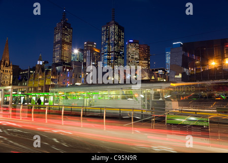 Traffico e tram sentieri di luce in Swanston Street con lo skyline della città in background. Melbourne, Victoria, Australia Foto Stock
