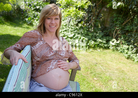 Donna incinta seduta su una panchina da giardino. Ella è di 35 settimane di gravidanza. Foto Stock