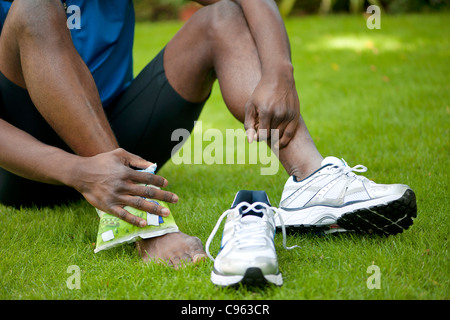 L'uomo applicando una confezione di ghiaccio per la sua caviglia infortunata. Foto Stock