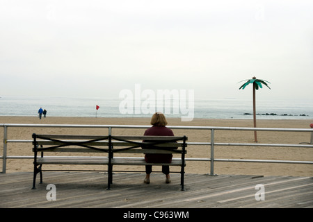 Una solitaria donna siede su un banco di lavoro sul Broadwalk, Spiaggia di Brighton, New York New York, Stati Uniti d'America. (C) Marc Jackson Foto Stock