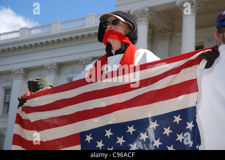 Protester tenendo un rialzo bandiera americana con sciarpa avvolta attorno alla bocca Foto Stock