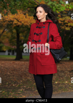 Moda autunno foto di una giovane e bella donna che cammina su un marciapiede con colori d'autunno alberi in background Foto Stock