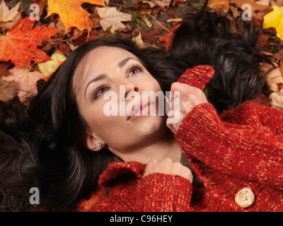 Bella donna con espressione sognante giacente sulla colorata caduta foglie Foto Stock