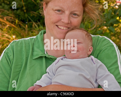 La famiglia naturale alla ricerca della madre, indossando nessun trucco, con testa rossa, tenendo il neonato 2 mesi di età infantile bambina. Foto Stock
