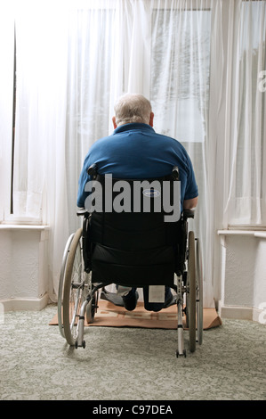 Anziani disabili uomo seduto nella sua sedia a rotelle guardando fuori della finestra Foto Stock