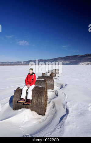 12 anni ragazza seduta su una balla di fieno in un campo (Ličko polje) durante la stagione invernale, Gorski Kotar, Croazia Foto Stock