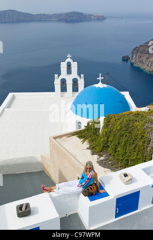 Donna relax su una parete al di sopra della chiesa ortodossa greca con una cupola blu, Fira, Santorini, Grecia, Europa Foto Stock