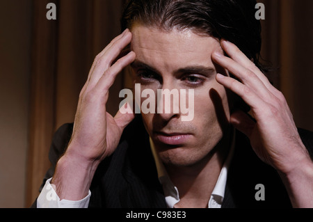 Sottolineato giovane uomo seduto alla scrivania e strofinando il suo tempio. Primo piano della faccia. Foto Stock