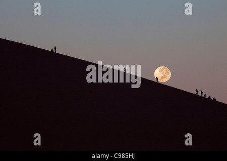 Turisti duna di arrampicata 45 all'alba con impostazione luna Foto Stock