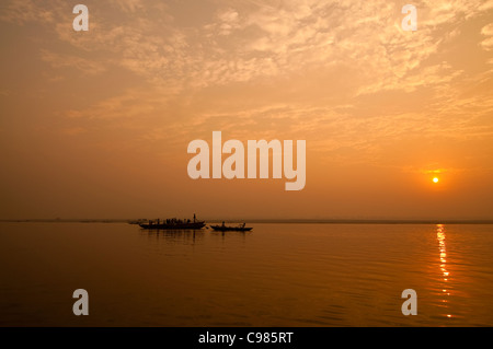 Un sunrise guardando oltre il più sacro dei fiumi in India. Il Gange. Sagome di barche di colline punteggiano l'orizzonte. Foto Stock