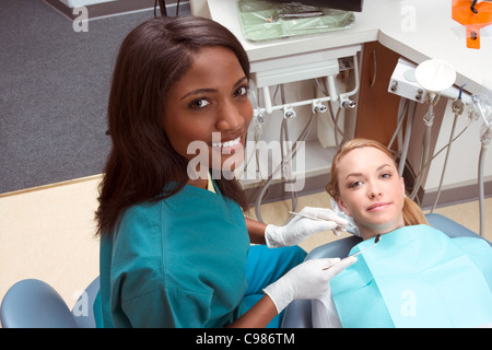 Giovane femmina caucasica bocca di apertura. Afro-americano di dentista etnica in bianco guanti in lattice controllare i suoi denti (focus su dentista) Foto Stock