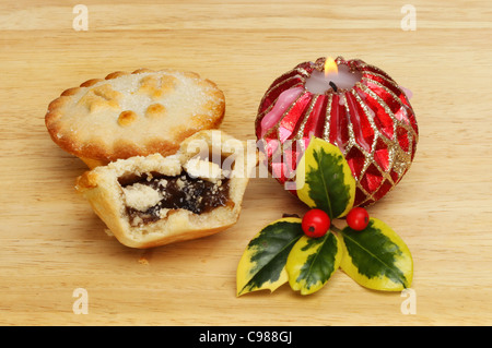 Tritare torte con un ardente cero decorativo e un rametto di fresco variegato holly su una tavola di legno Foto Stock