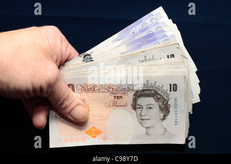 Un batuffolo di £10, £20 Note ventaglio e tenuto in mano tra il pollice e le dita Foto Stock