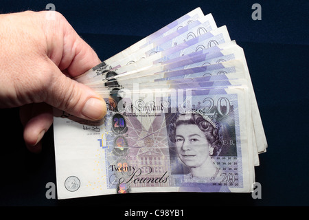 Un batuffolo di £20 Note ventaglio e tenuto in mano tra il pollice e le dita Foto Stock
