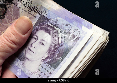 Un batuffolo di £20 note piegato tenuto in mano tra il pollice e le dita Foto Stock