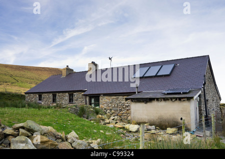 Remote cottage rurale con pannelli solari sul tetto per il riscaldamento di acqua calda e la generazione di energia elettrica con una piccola turbina eolica la filatura Foto Stock