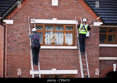 Gli uomini sulle scale a pioli  polistirene Casa Tallone parete di cavità di isolamento, lavoratori nel cablaggio di sicurezza, installazione di isolamento in schiuma a Southport, Regno Unito Foto Stock