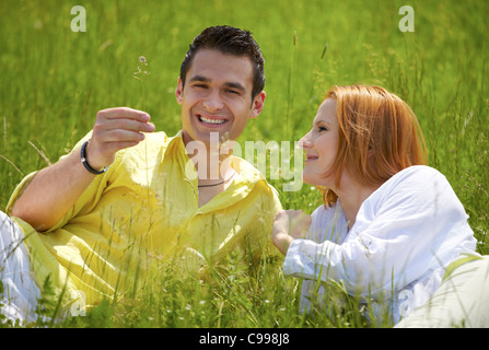 Felice coppia giovane godendo una giornata all'aperto seduto in un campo di erba. Foto Stock
