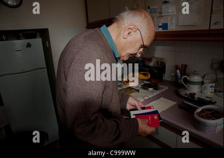 Un uomo anziano a contare i suoi risparmi libri nella cucina di casa sua. Foto Stock