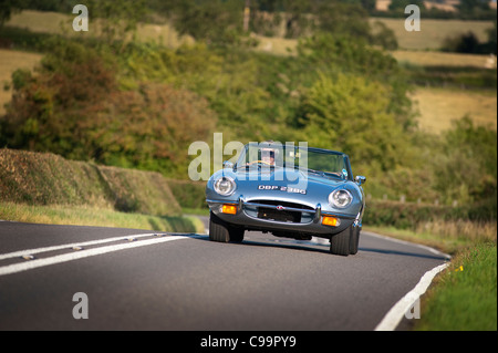 Jaguar E-Type auto sportiva essendo pilotati attraverso Inghilterra rurale in estate. Foto Stock